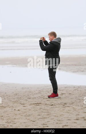 Young man taking photograph on his iPhone on Black rock sands beach Stock Photo