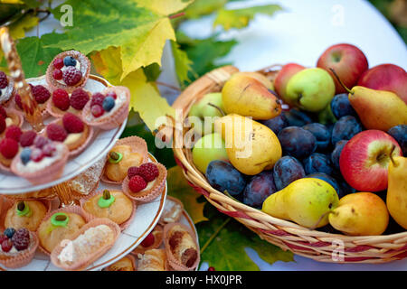 Still life of fresh fruit in the basket pastries and tartlets on a plate with autumn leaves of maple Stock Photo