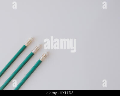 Three identical pencils lying on a plain background. (Rubbers) Stock Photo