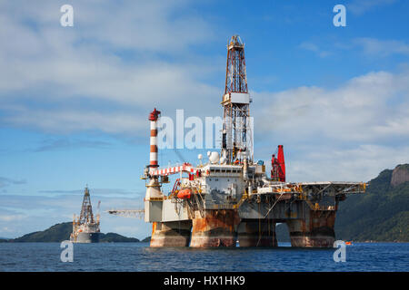 Offshore oil rig in front of green mountains with a blue sky above. Stock Photo