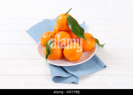 plate of fresh tangerines with leaves on blue place mat Stock Photo