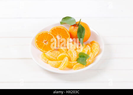 whole and sliced tangerines on white plate Stock Photo