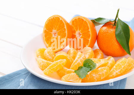 whole and sliced tangerines on white plate - close up Stock Photo