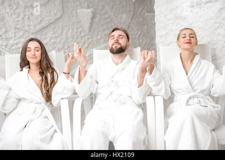 Three friends in bathrobes meditating in the salt room Stock Photo