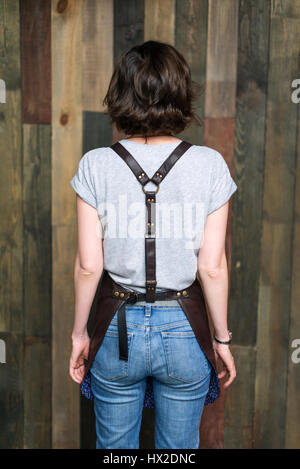 Young woman chef or waiter posing, wearing apron and t-shirt on wooden background. Stock Photo