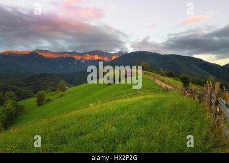 Beautiful sunset with green fields and sunlit mountain range in the background photographed in Transylvania near Brasov on a beautiful hilly setting Stock Photo