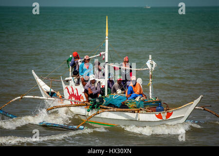 Overloaded Filipino fishing boat filled with men and teen boys makes a landing on BayBay Beach in Roxas City, Panay Island, Philippines. Stock Photo
