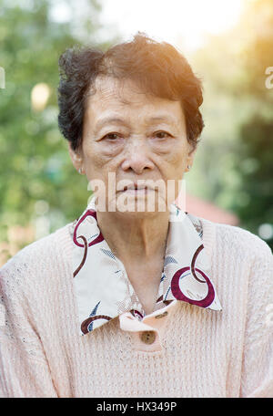 Portrait of upset Asian senior adult woman at outdoor garden park in the morning. Stock Photo