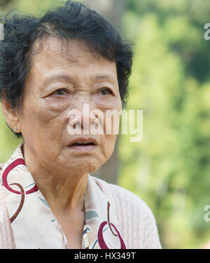 Portrait of worried Asian senior adult woman at outdoor garden park in the morning. Stock Photo