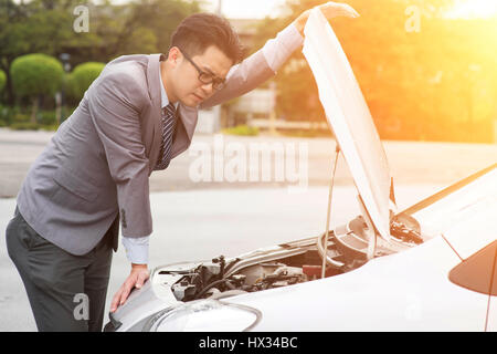 Young Asian business man looking under the hood of breakdown car. Stock Photo