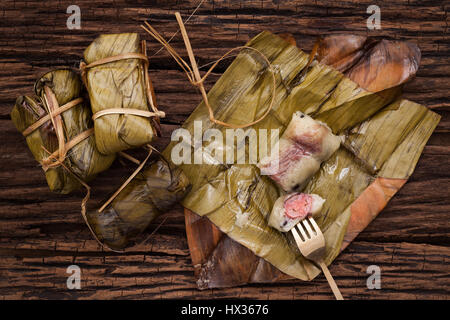 Khao Tom Mat - Thai dessert - Sticky Rice, Banana and Black Beans Wrapped in Banana leaf - Still life close up on wooden background Stock Photo