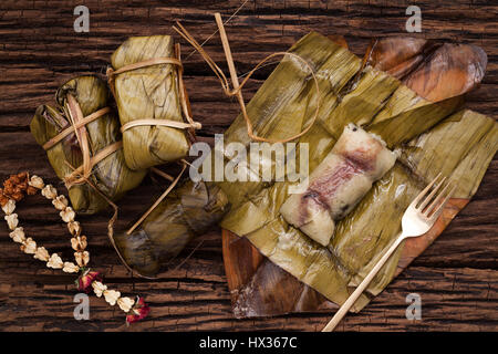 Khao Tom Mat - Thai dessert - Sticky Rice, Banana and Black Beans Wrapped in Banana leaf - Still life close up on wooden background Stock Photo