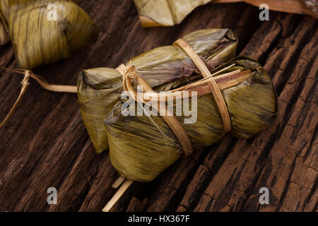 Khao Tom Mat - Thai dessert - Sticky Rice, Banana and Black Beans Wrapped in Banana leaf - Still life close up on wooden background Stock Photo