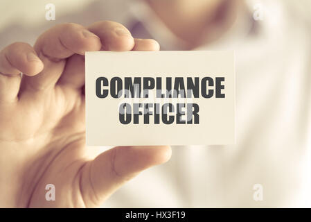 Closeup on businessman holding a card with text COMPLIANCE OFFICER, business concept image with soft focus background and vintage tone Stock Photo