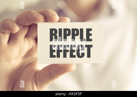 Closeup on businessman holding a card with text RIPPLE EFFECT, business concept image with soft focus background and vintage tone Stock Photo