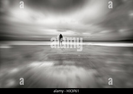 Silhouette of person standing head down on deserted beach in wintertime, motion blur. Stock Photo