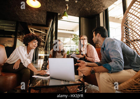 Business team sitting in office lobby and having a brainstorming session. Happy corporate business people sitting together with laptop and discussing. Stock Photo