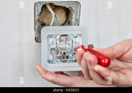 Replacing electric wall light switch, connection to the electrical wiring, tightening the screw using a screwdriver. Stock Photo