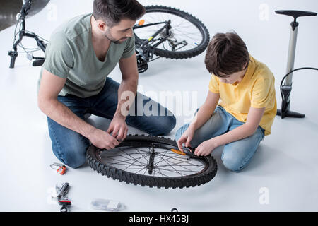 Son and father repairing bicycle tire in studio on white Stock Photo