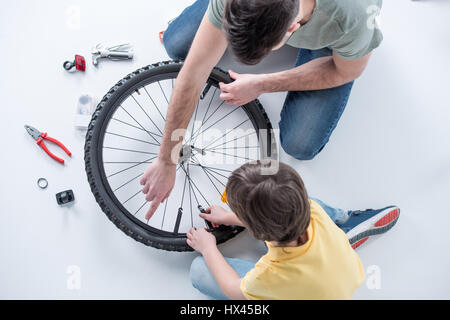 overhead view of son and father repairing bicycle tire in studio on white Stock Photo