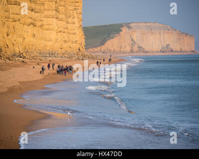 West Bay, Dorset, UK. 24th March 2017. People enjoying the sun below the East Cliff as the cloud finally clears and a hazy but sunny afternoon follows. With a weather high set to follow and warmer temperatures expected for this weekend. © Dan Tucker/Alamy Live News