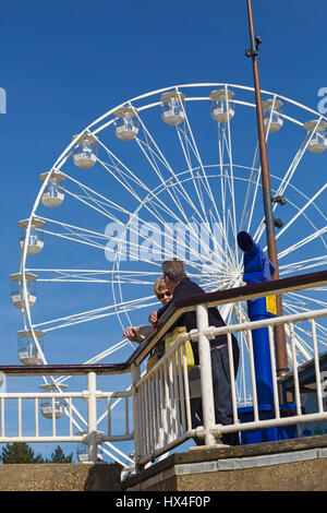 Bournemouth, Dorset, UK. 25 March 2017. UK weather: lovely warm sunny day as visitors head to the seaside to make the most of the sunshine at Bournemouth beaches. The big wheel returns to Bournemouth for the summer to attract visitors. Couple standing on Bournemouth Pier next to talking telescope with the big wheel towering behind. Credit: Carolyn Jenkins/Alamy Live News Stock Photo