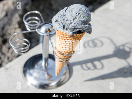 Stuttgart, Germany. 23rd Mar, 2017. An ice cream cone with a scoop of 'Beton & Asphalt' (Concrete & asphalt) seen on concrete blocks at the construction site, which inspired the owners of the ice cream parlor to create this special ice cream flavour, in Stuttgart, Germany, 23 March 2017. The owners named the ice cream flavour consisting of vanilla ice cream infused with edible coal 'Beton & Asphalt' (lit. Concrete & asphalt) as a joke due to a construction site in front of their establishment. Now it will be made available permanently. Photo: Lino Mirgeler/dpa/Ģ����ý Live News Stock Photo