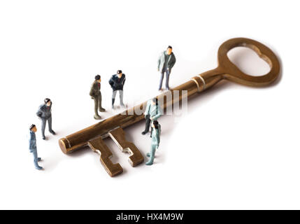 Group of miniature figures standing around giant brass key on white background Stock Photo