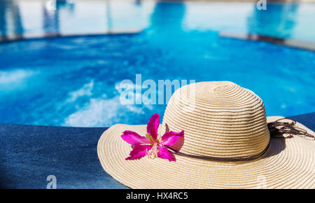 Straw hat and tropical flower near swimming pool Stock Photo - Alamy