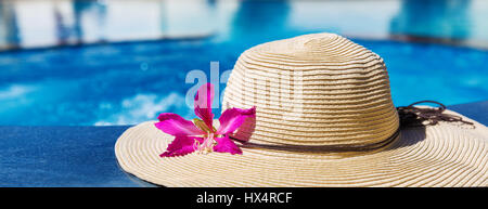 Straw hat with orchid flower near swimming pool - holiday concept Stock Photo