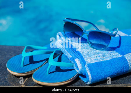 Blue slippers and sun glasses near swimming pool - holiday concept Stock Photo