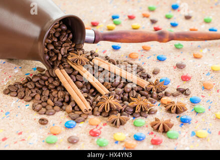 A tumbled clay jezva jar filled with coffee beans, anise and cinnamon sticks with colorful candies Stock Photo