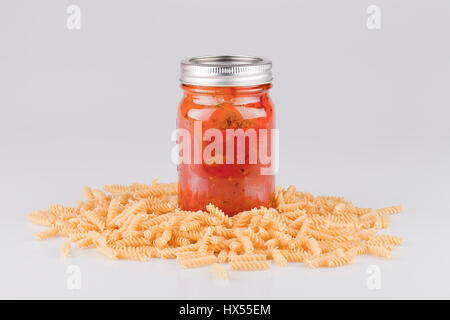 Jar of spaghetti sauce and fusillis on a white surface. Isolated on white background. Stock Photo