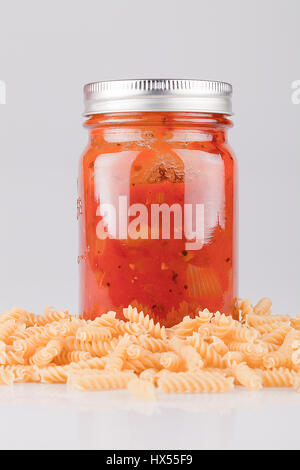 Jar of spaghetti sauce and fusillis on a white surface. Isolated on white background. Stock Photo