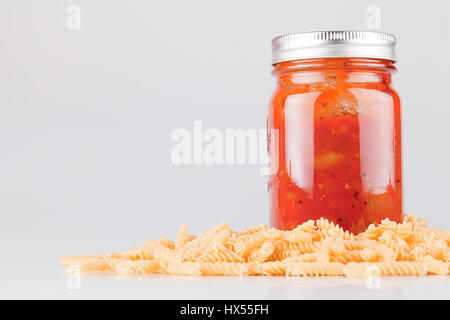 Jar of spaghetti sauce and fusillis on a white surface. Isolated on white background. Stock Photo