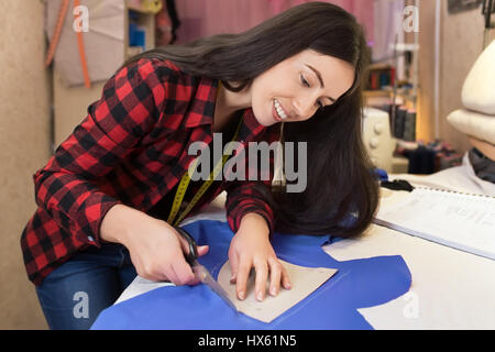 young woman seamstress cutting fabric on the sketch lines with use scissors. Girl working with a sewing pattern. Hobby sewing as a small business conc Stock Photo