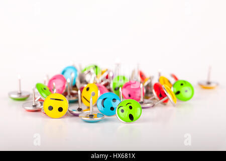 Pile of colorful smiley pushpins on a white surface. Pile of smiley thumbtacks isolated on white background. Stock Photo
