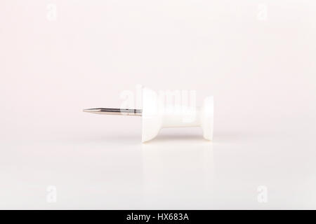 White pushpin on a white surface. Push pin isolated on white background. Stock Photo