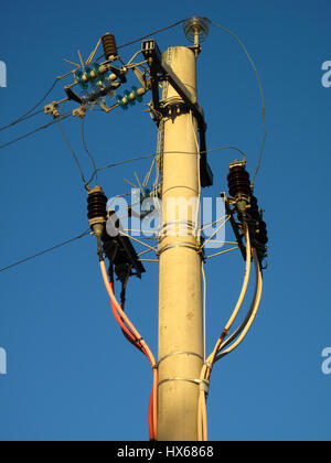 An old electric pole wit many wires connected on a blue sky background Stock Photo