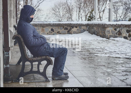 Man sitting on bench in winter with snow on the ground Stock Photo