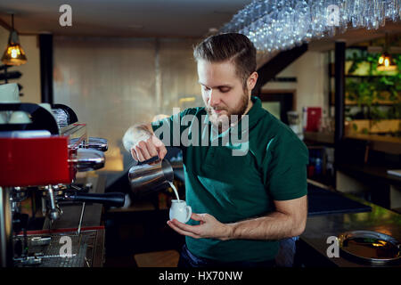 The bartender barista pours  hot milk into a glass in  bar cafe  Stock Photo