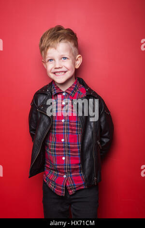 Fashion little boy wearing a leather jacket. Studio portrait over red background Stock Photo
