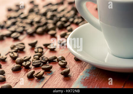 Roasted coffee beans on painted wooden board with white espresso cup and saucer Stock Photo