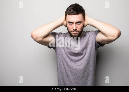 Shocked dazed young man in plaid shirt holding head with both hands over grey background Stock Photo