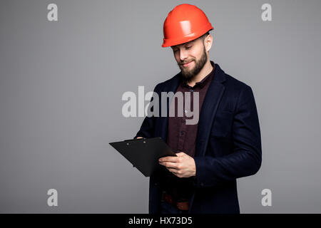 Caucasian man in a black suit and construction helmet holding black folder Stock Photo