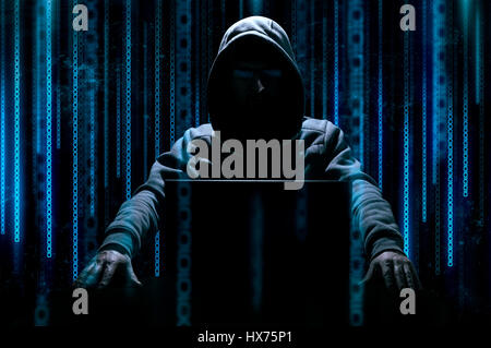 Hacker sits behind laptop with binary code on background Stock Photo