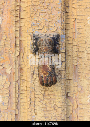Hand shaped door knocker on an old wooden door with flaking paint, Spain Stock Photo