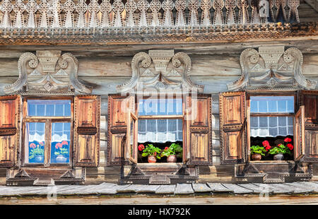Windows of old traditional Russian log house with carved wooden trim and red geranium flowers Stock Photo