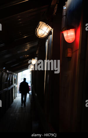 Man walking into the light through a dark tunnel. In the foreground there are two red and white lamps Stock Photo