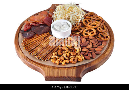 Cocktail of beer snacks on round wooden board with handles, cheese, nuts, pretzels, straw and dried meat isolated on white background. Stock Photo